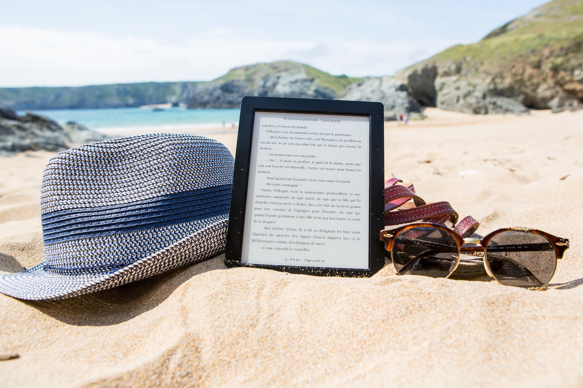 Hat, eReader and sunglasses on beach sand
