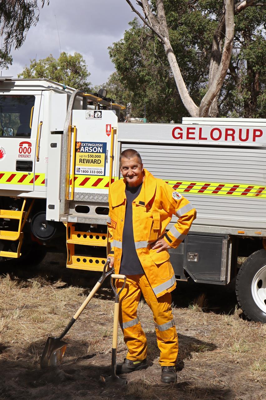 Man standing in front of a fire truck, dressed in yellow work wear.